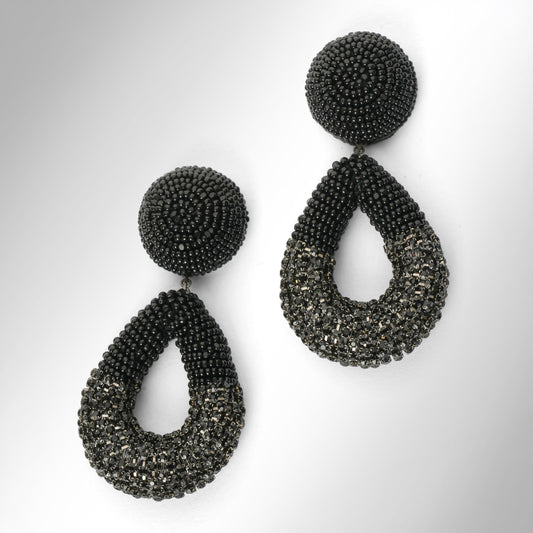 A pair of large statement dangle earrings made from black beads and chainstone, featuring a round stud top and a teardrop-shaped drop, shown on a light gray gradient background.
