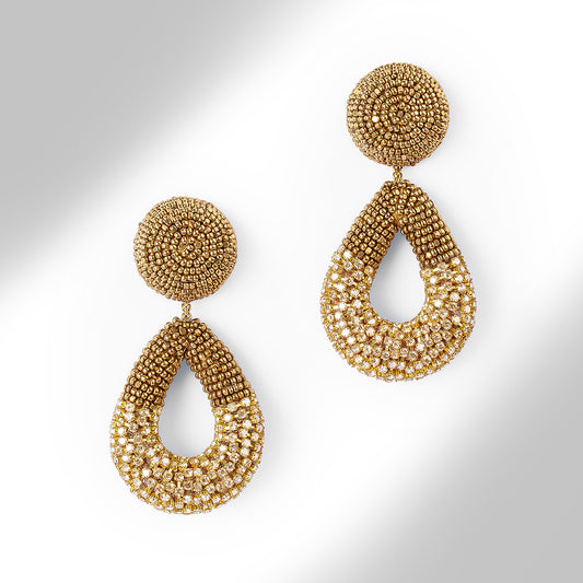A pair of large statement dangle earrings made from gold tone beads and chainstone, featuring a round stud top and a teardrop-shaped drop, shown on a light gray gradient background.