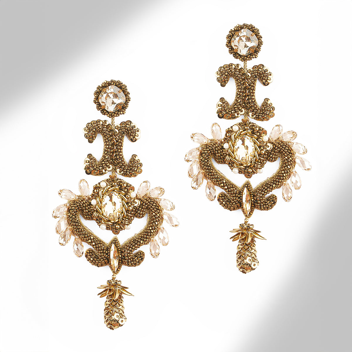 A pair of ornate gold-tone statement earrings with intricate beaded scrollwork and gold stone accents, displayed on a light gray background.