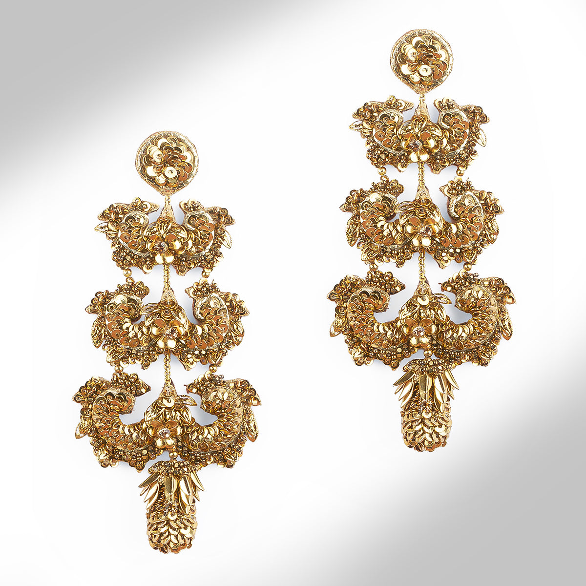 A pair of ornate gold-toned earrings with intricate floral and leaf-like sculpted details, shown on a plain light gray background. 