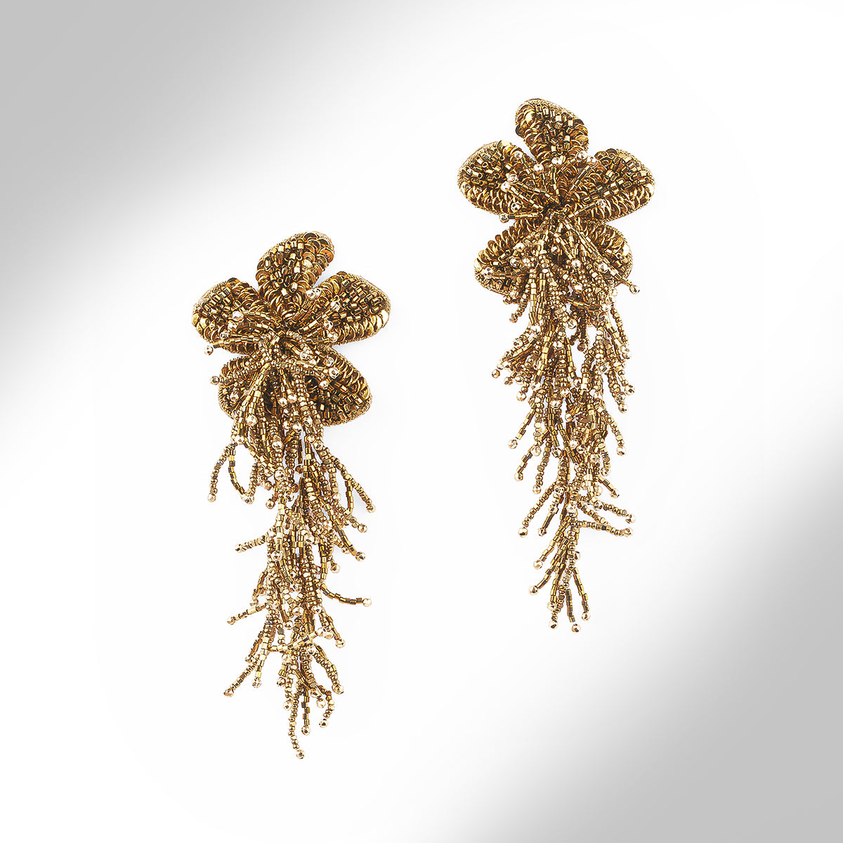 A pair of ornate gold-tone beaded earrings with a floral cluster at the top and cascading, branch-like beadwork hanging below, shown on a plain light background.
