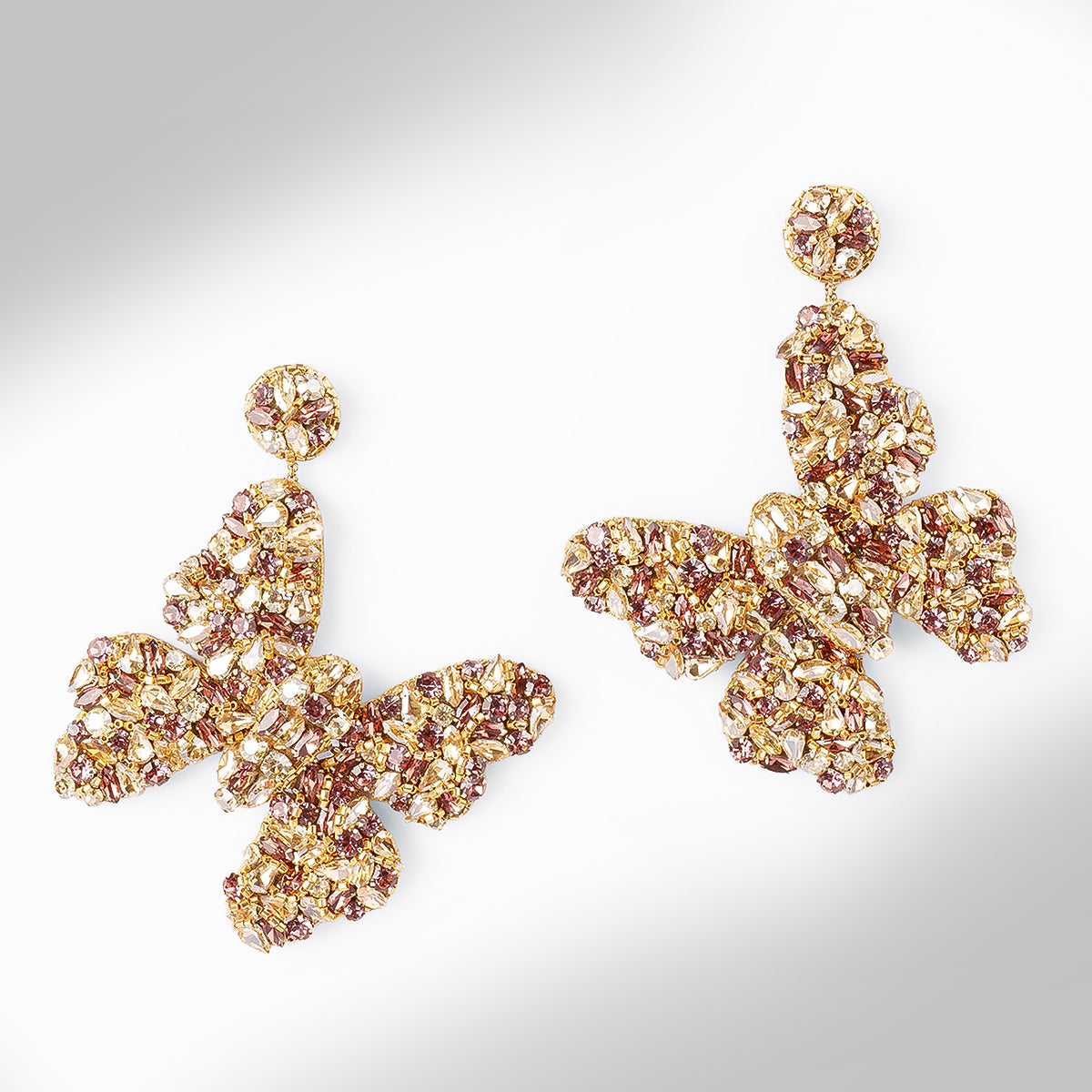 A pair of butterfly-shaped drop earrings made of gold-toned metal and clear faceted stones, arranged on a light gray gradient background.
