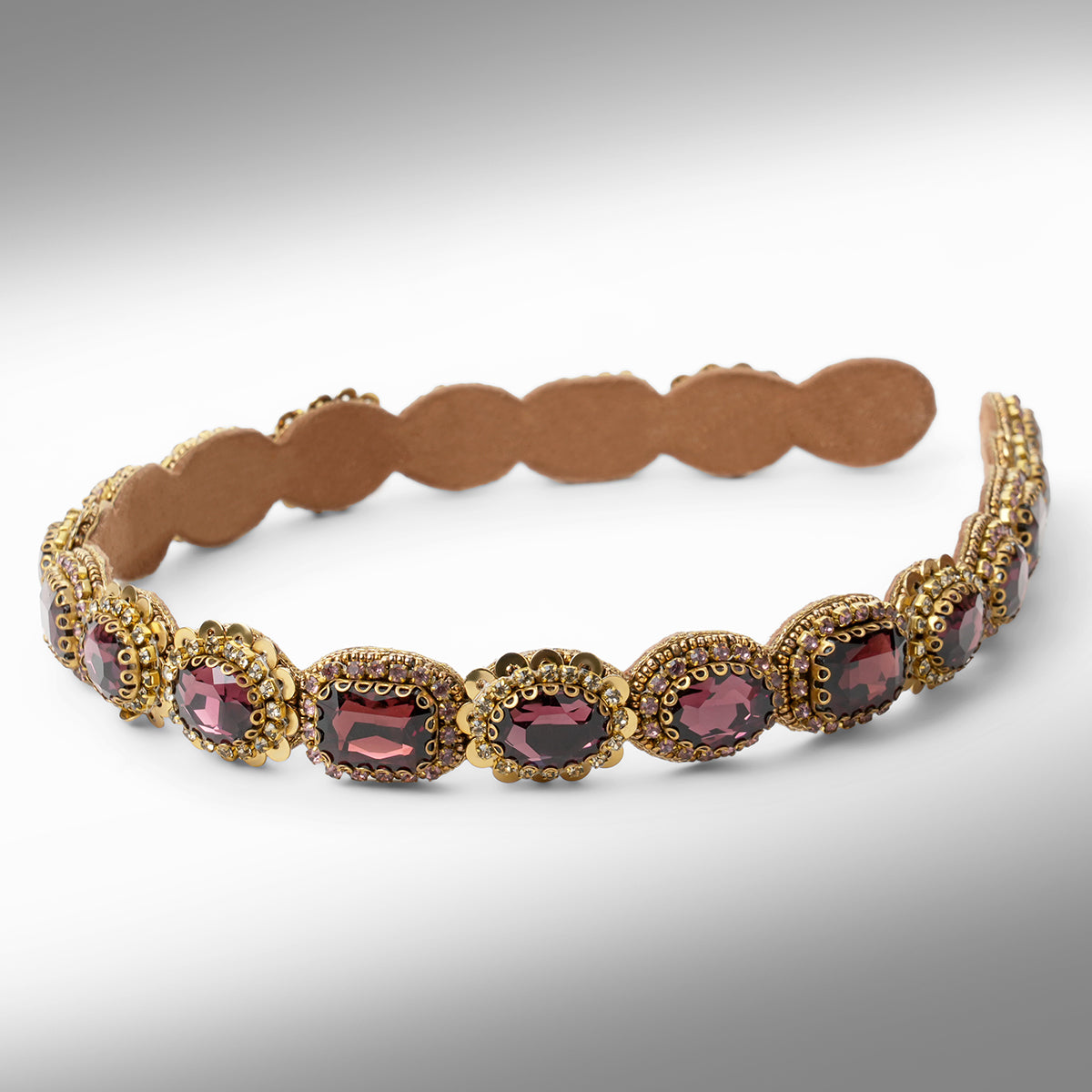 A gold-toned scalloped hard headband featuring oval burgundy stones in ornate settings, displayed on a neutral gray background.