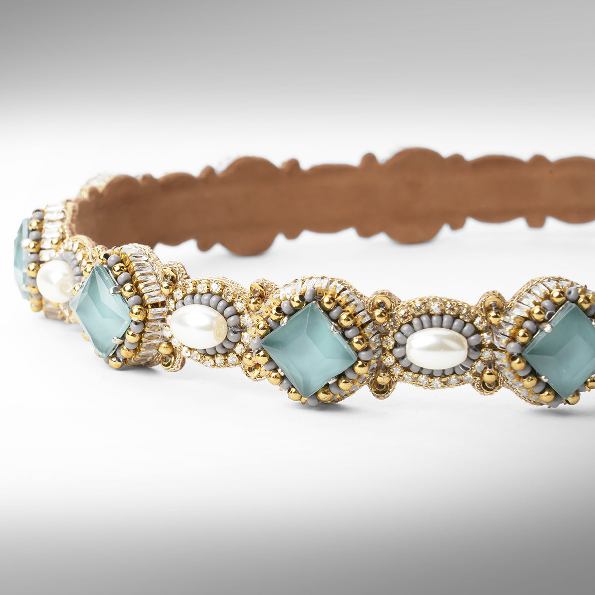 A close-up of a beaded headband with scalloped edges, featuring grey stones, white faux pearls, and gold and silver beads on a neutral gray background.
