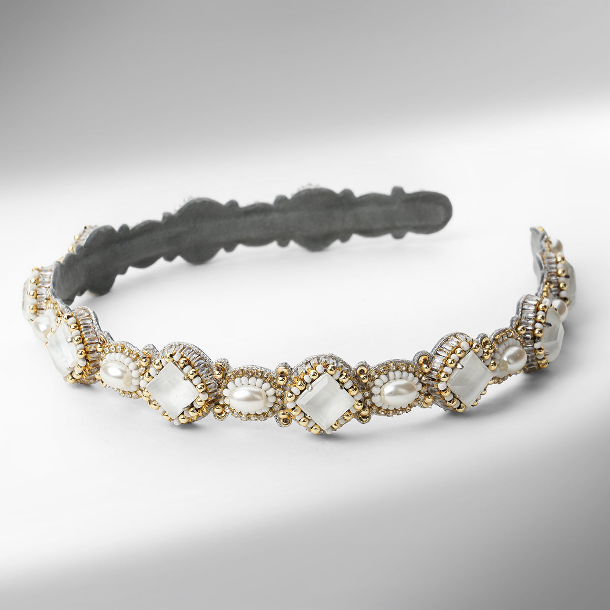 A beaded headband with scalloped edges, featuring white stones, white faux pearls, and gold and silver beads on a neutral gray background.