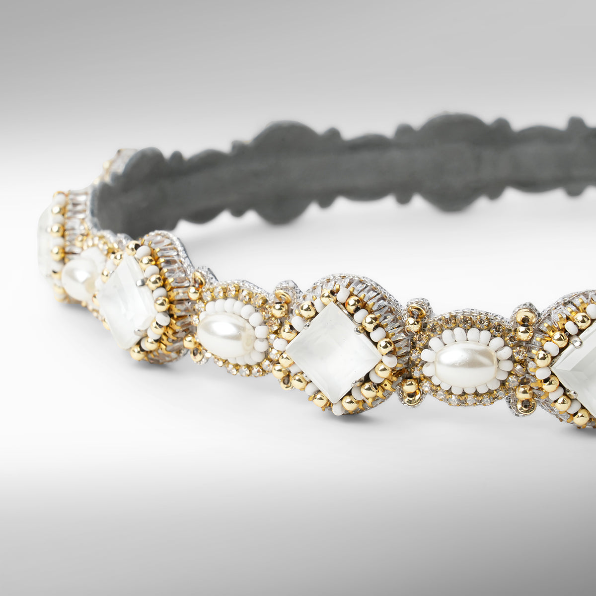 A close-up of a beaded headband with scalloped edges, featuring white stones, white faux pearls, and gold and silver beads on a neutral gray background.