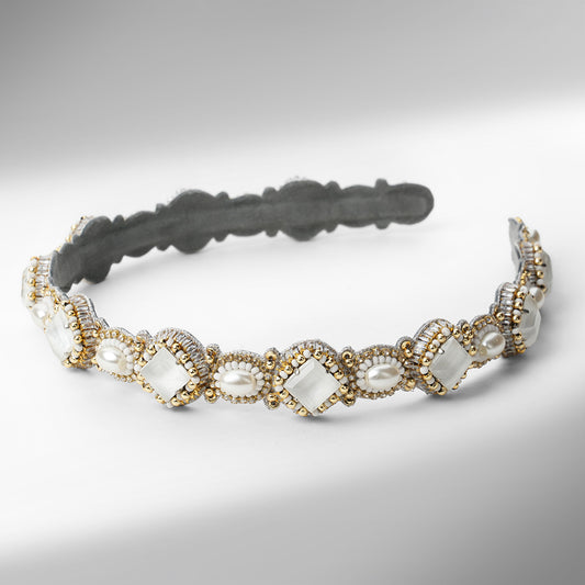A beaded headband with scalloped edges, featuring white stones, white faux pearls, and gold and silver beads on a neutral gray background.