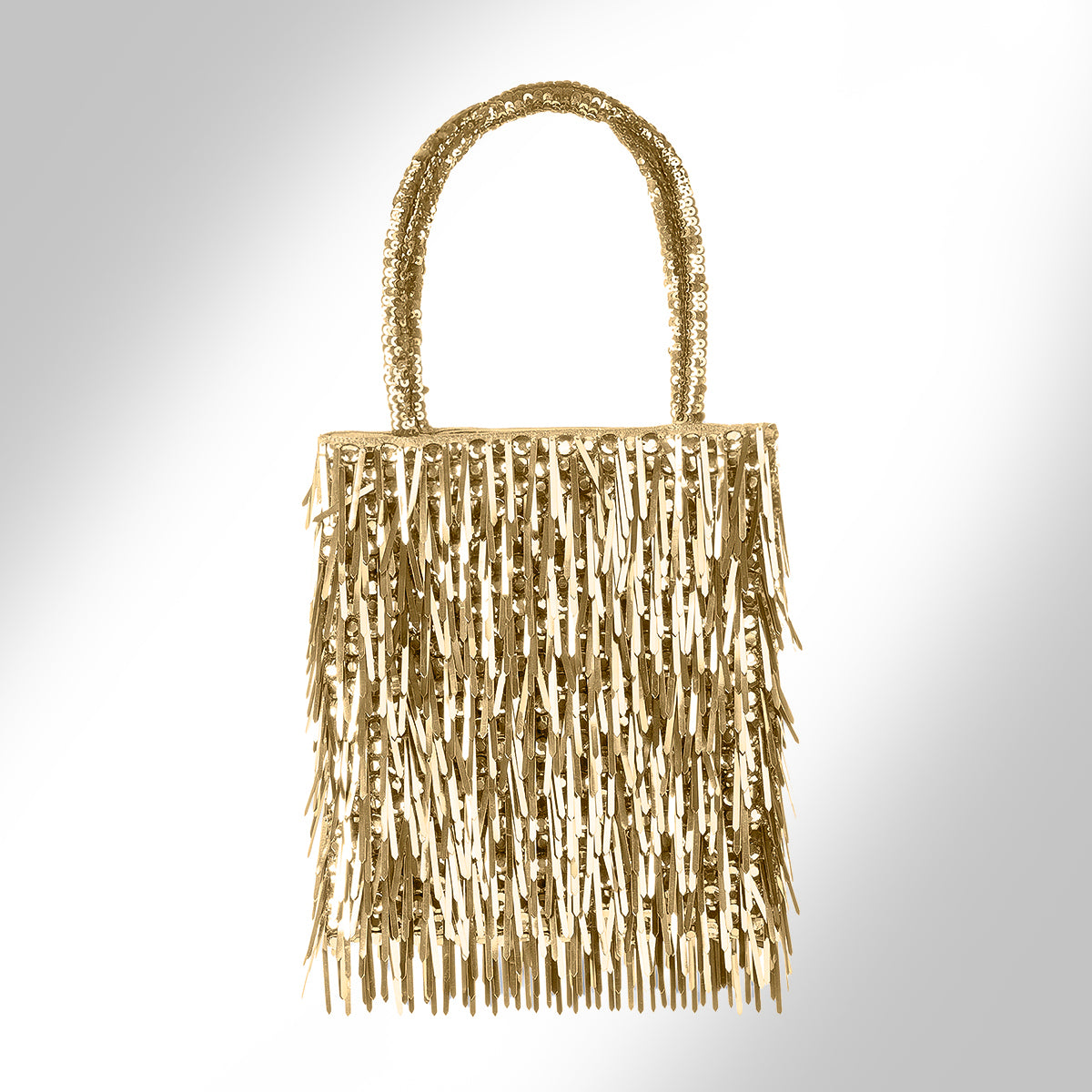 A gold metallic fringe handbag, photographed against a light gray gradient background.